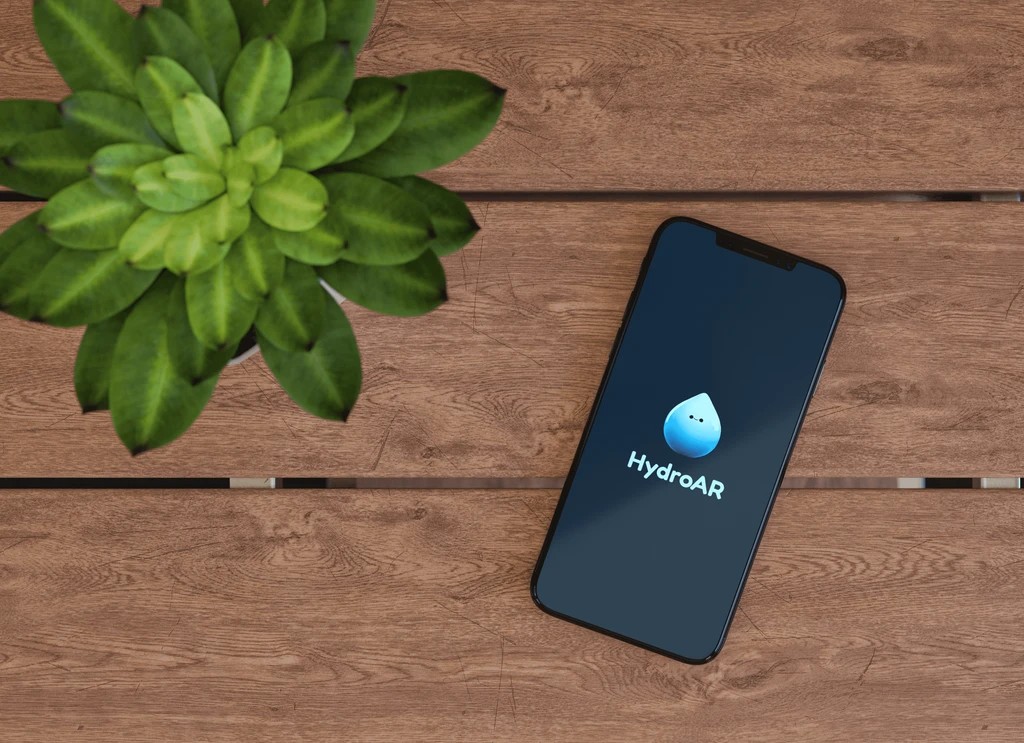 HydroAR splash screen on a smartphone resting on a wooden table beside a potted succulent plant